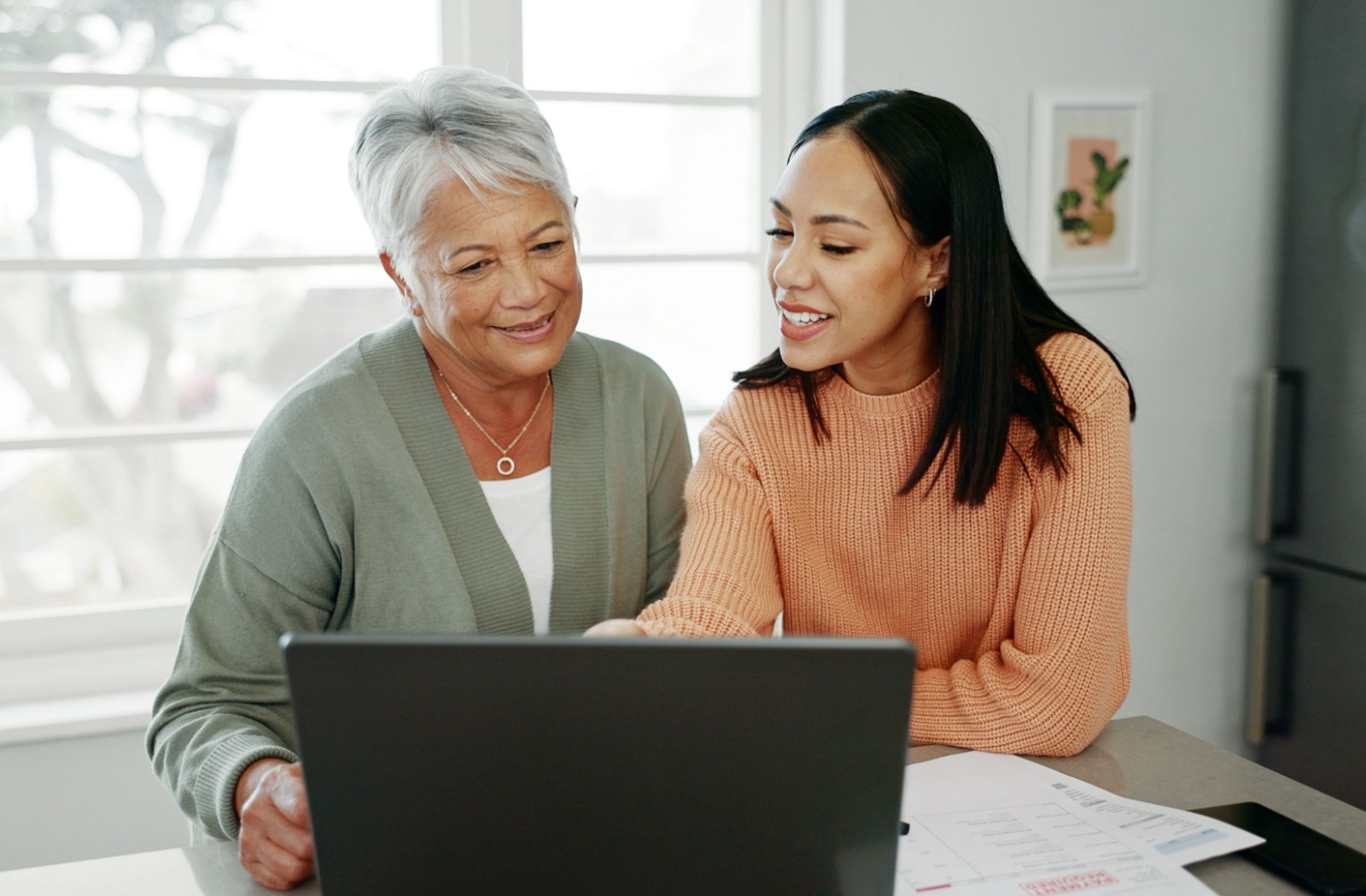 A younger adult helping an older adult use a laptop while discussing care options