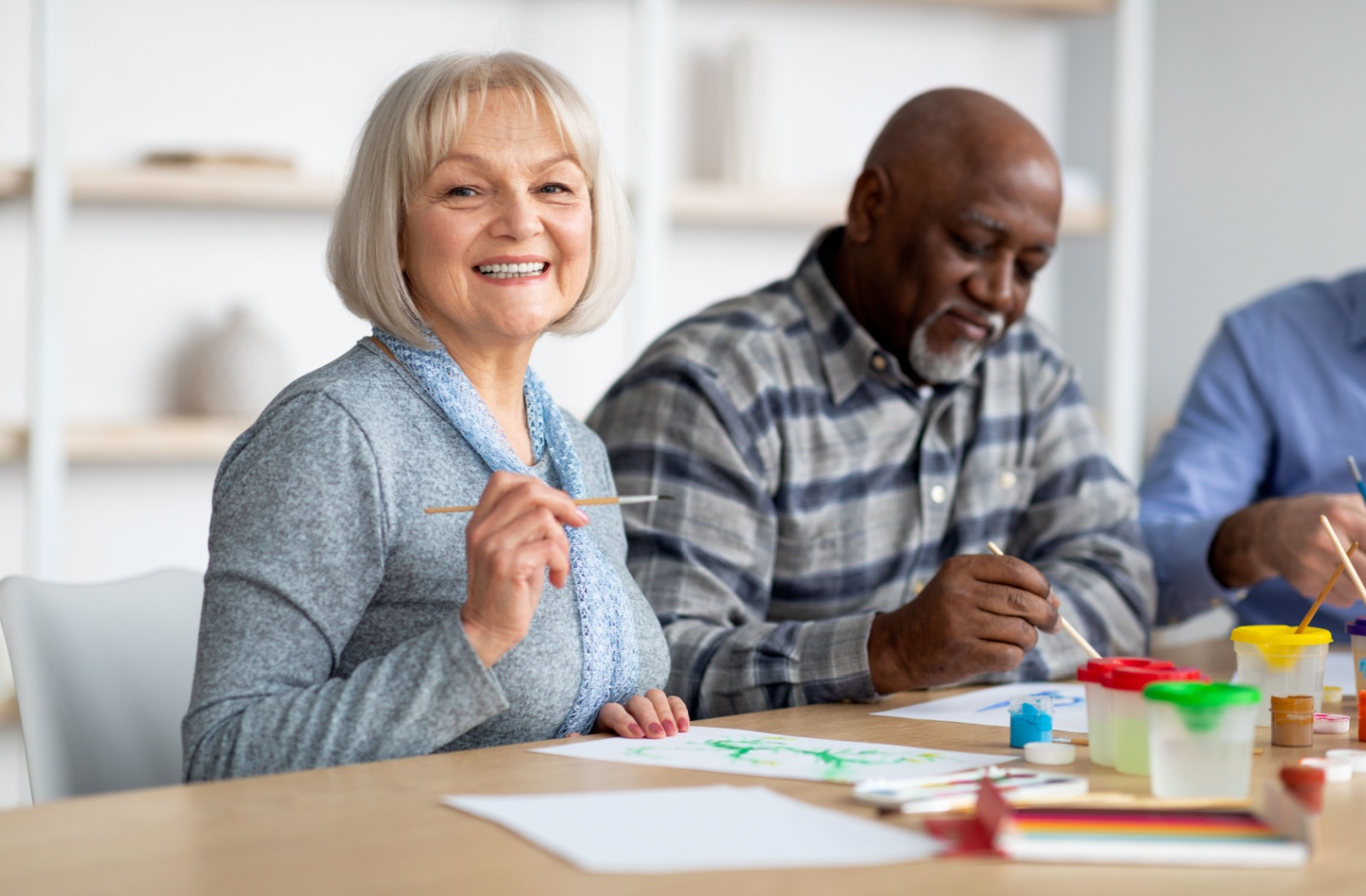 A senior in assisted living painting on a canvas while enjoying time with friends