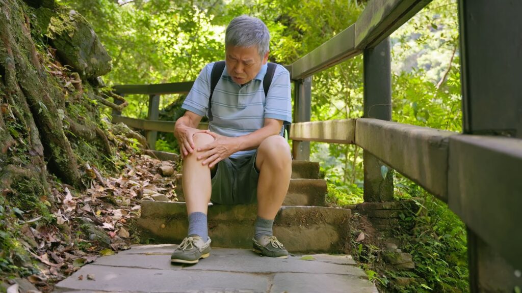 Senior sitting down after hurting their knee on a trail hike.